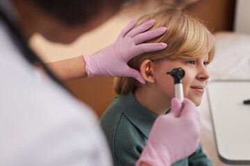 Side view close up of unrecognizable doctor examining childs ears and hearing in clinic