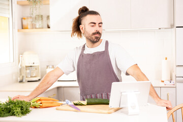 Fototapeta na wymiar long-haired man cooking at home looking at tablet, chopping vegetables