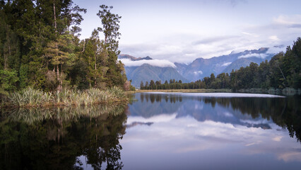 Beautiful lake surrounded by exotic forest and mountains in background during sunset, New Zealand