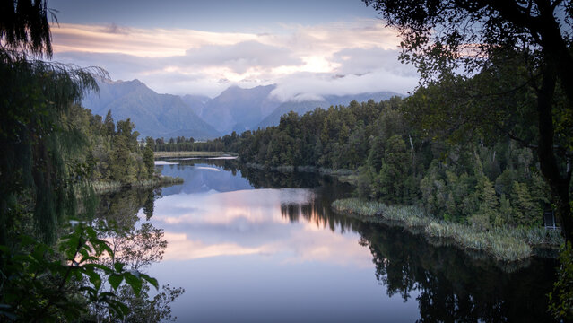Beautiful colorful sunset over a lake surrounded by forest and mountains in backdrop in New Zealand