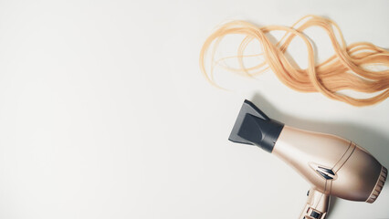 Piece of wavy blonde hair and a  hair dryer with copy space on the white background. Hairdresser concept.