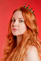 Portrait of a red-haired young woman with a crown on her head on a scarlet background - 752106665