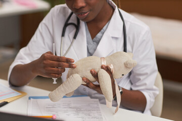 Close up of pediatric doctor explaining antibiotics injection using toy bear, copy space