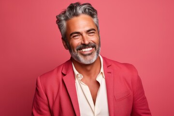 Portrait of a handsome mature Indian man with gray hair and beard smiling at the camera while standing against pink background