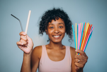 A cheerful woman presents a choice between a single reusable straw and a bundle of colorful plastic...
