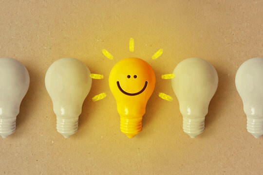 Glowing yellow light bulb with smile and white light bulb turned off - Positive thinking and standing out from crowd concept