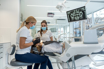 female dentist adjusts  dental surgical lamp  young girl patient lying on the dental chair.