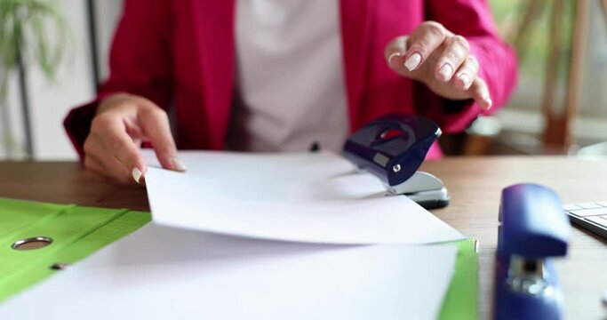 Businesswoman hand punch paper on table. Secretary manager makes holes in paper with puncher