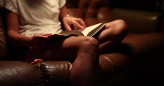 Closeup ofa woman hands sitting on sofa and reading book at home in evening. Interesting book reading and education
