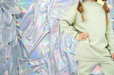 Girl in Casual Green Tracksuit on Holographic Background. Half-length portrait of a girl with two braids, wearing a light green tracksuit, standing confidently against a shiny, holographic background