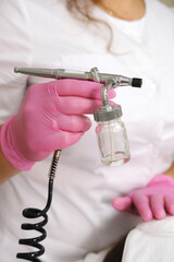 Cosmetologist Holding Airbrush for Skincare Treatment.A cosmetologist's hand in a pink glove holds a professional airbrush tool for a precision skincare application. 