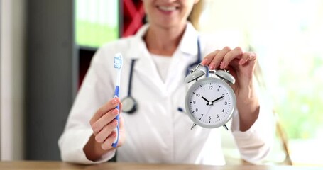 Dentist doctor holds toothbrush and alarm clock in hands during oral hygiene. Dentist working in dental hospital