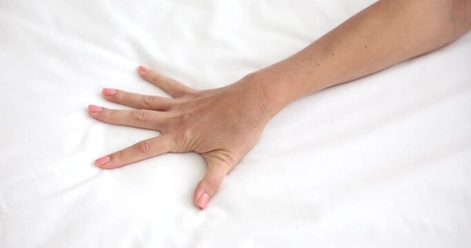 Woman hand passionately clutches sheet on bed. Closeness of young woman on bed