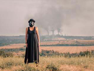 young girl in a black dress and gas mask on the background of smoking factory chimneys in Ukraine