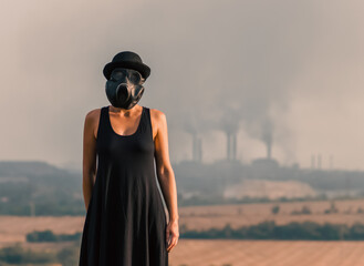 young girl in a black dress and gas mask on the background of smoking factory chimneys in Ukraine...