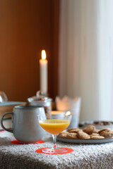 Obraz na płótnie Canvas Cup of tea or coffee, stack of books, e-reader, glasses, various cookies, almonds, orange juice and lit candles on the table. Hygge at home. Selective focus.