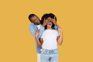 A playful African American man surprises a woman by covering her eyes from behind