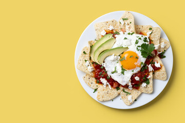 Traditional Mexican breakfast red chilaquiles with egg on yellow background. Top view. Copy space
