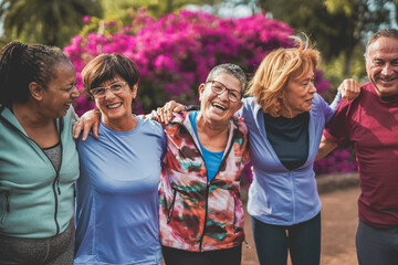Group of multiracial senior people having fun hugging each other after sport workout at city park - Healthy lifestyle concept