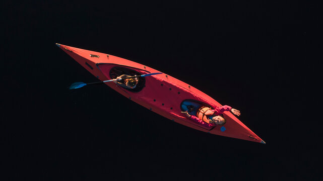 A person in a red kayak floats on tranquil waters, the deep blue of the lake contrasting with the vibrant hue of the vessel. The image evokes a sense of peace and oneness with nature.