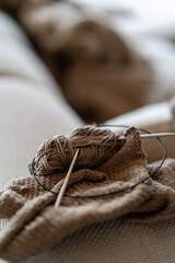 Knitting needles and yarn in beige color and environment, indoor living room, with natural lighting.