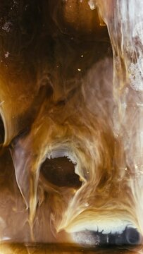 Coffee creamer or milk being poured into a cup of iced coffee.  Closeup vertical video in slow motion.