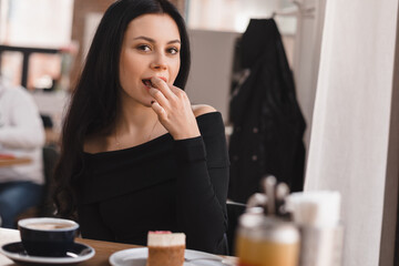 Brunette woman rest in cafe eating cheesecake, enjoy of delicious taste, cup of coffee on table.