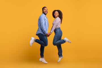 Happy young black couple holding hands and jumping in unison
