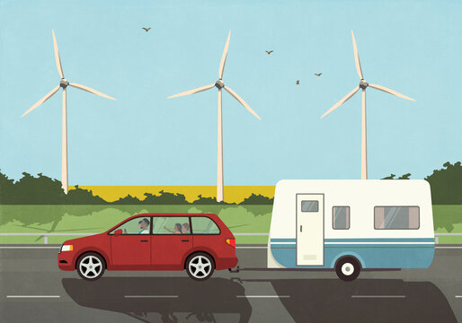 Family in car on vacation pulling camper trailer, driving past wind turbines in idyllic countryside
