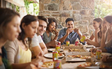Poster Friends, group and eating of pizza in house with happiness, soda and social gathering for bonding in dining room. Men, women and fast food with smile, drinks and diversity at table in lounge of home © Mikolette Moller/peopleimages.com