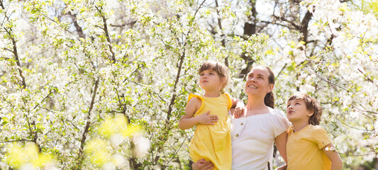 mom and two children  embrace amid flowering in garden in summer.  stress relief. Spring awakening. Slow life. Enjoying the little things. Dreaming of spring.  banner