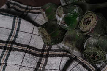 fresh frozen baby artichoke buds raw on kitchen cloth textle, wooden board, dark rustic colors, ready to cook