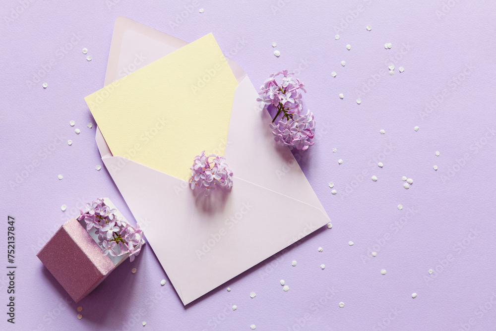 Sticker Lilac flowers, envelope and gift box over purple paper background. Flat lay, top view. Lovers or Women's day. Minimal floral frame made of flowers. Blank greeting card mockup. 