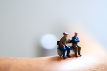 Miniature people, sitting on a bench and on a fence in a house.