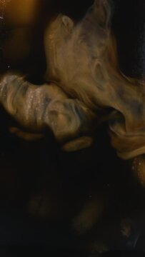 Coffee creamer or milk being poured into a cup of iced coffee.  Closeup vertical video in slow motion.
