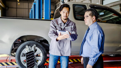 Asian automotive mechanic use tablet explain car condition to client in garage. Vehicle service...