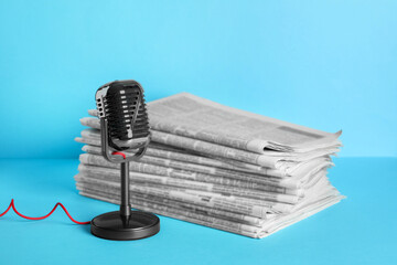 Newspapers and vintage microphone on light blue background. Journalist's work