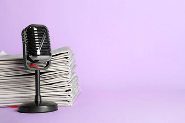 Newspapers and vintage microphone on light violet background, space for text. Journalist's work