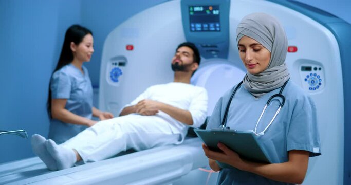 Arabian doctor with stethoscope holding folder. Muslim doctor in hijab preparing for procedure. Nurse giving instructions to patient. Clinic of magnetic resonance tomography. CT scanner.