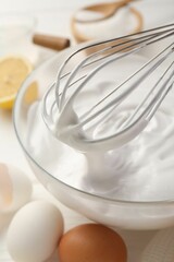 Bowl with whipped cream, whisk and ingredients on white wooden table, closeup