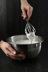 Woman making whipped cream with whisk at black table, closeup