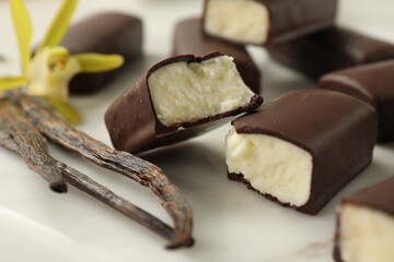 Glazed curd cheese bars, vanilla pods and flower on white board, closeup