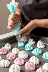 Woman hands squeeze colored meringue on a baking sheet to be baked
