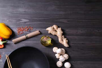 Empty iron wok, chopsticks and ingredients on dark grey wooden table, flat lay. Space for text