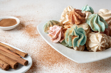 French meringues decorated with cinnamon sprinkled on a white background accompanied by cinnamon sticks