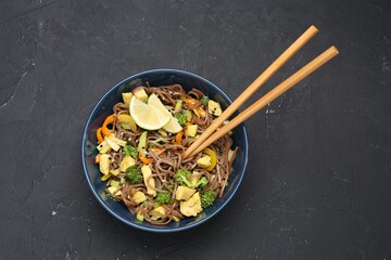 Stir-fry. Delicious cooked noodles with chicken and vegetables in bowl served on gray textured table, top view