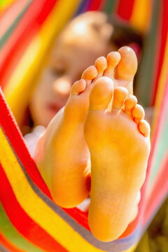 Young beautiful girl resting in comfortable hammock at green garden. Selectve focus on bare feet