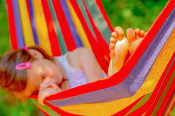 Fototapeta na wymiar Young beautiful girl sleeping in a hammock with bare feet, relaxing and enjoying a lovely sunny summer day. Safety and happy childhood and leisure concept. Selective focus on bare feet
