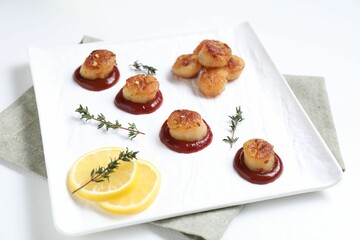 Delicious fried scallops with tomato sauce and lemon served on white table