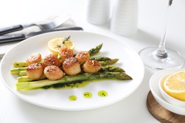 Delicious fried scallops with asparagus, lemon and thyme served on white table